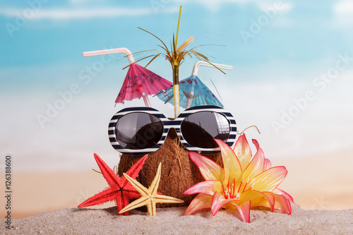 Coconut, sunglasses, starfish and flower in the sand against sea.