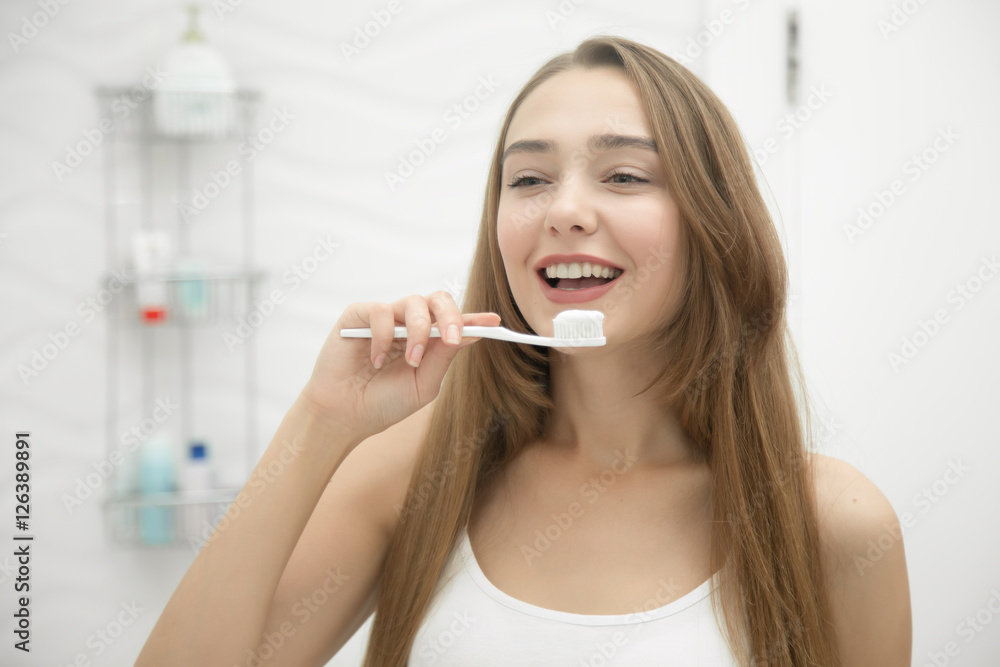 Portrait of a young smiling girl cleaning her teeth, looking at the bathroom mirror. Lifestyle, beauty concept photo Portrait of a young smiling girl cleaning her teeth, looking at the bathroom mirror. Lifestyle, beauty concept photo