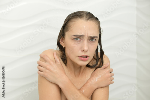 Young woman shivering with cold in the shower, the water is turned off, embracing her shoulders. Beauty concept photo photo