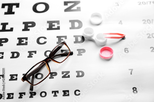 Glasses, lenses container and pincer on eye test chart, close up view. Healthy eyes concept