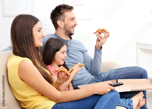 Happy family eating pizza and watching TV at home