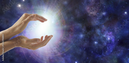 Life Force Energy - side view of female cupped hands with a bright vortexing burst of light on a dark blue deep space background with copy space to the right