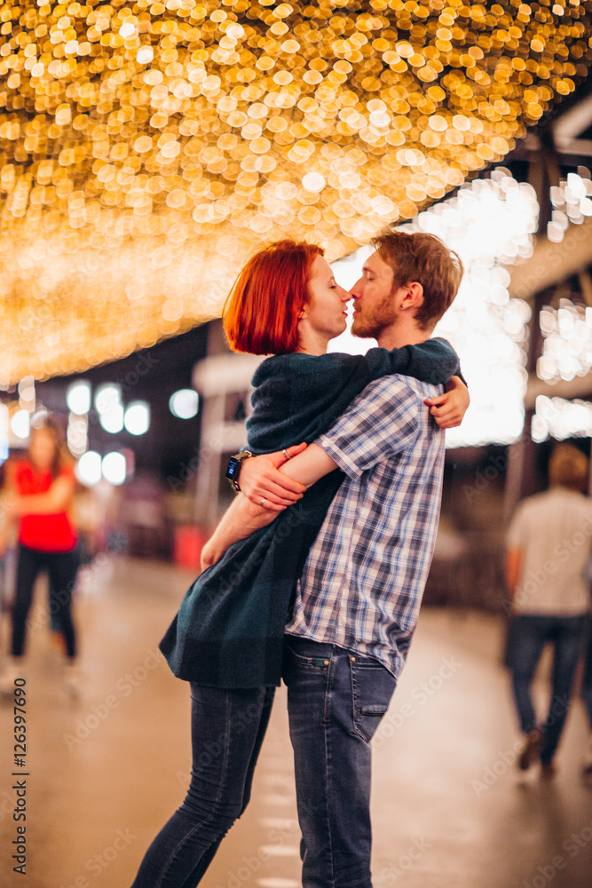 Happy couple embracing and kissing in the evening on a light garlands