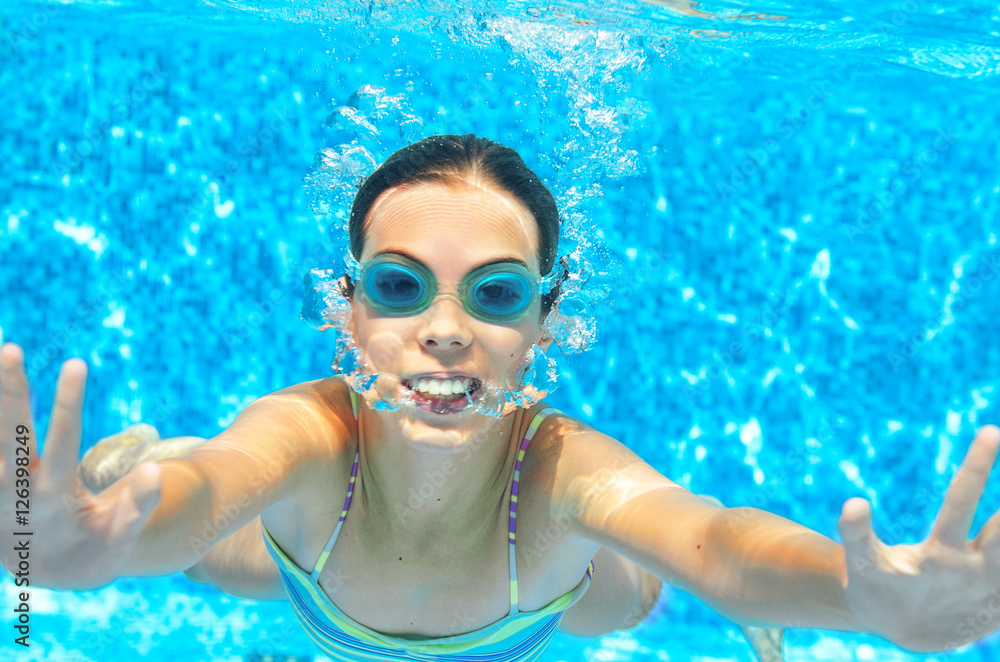 Naklejka premium Child swims in pool underwater, funny happy girl in goggles has fun under water and makes bubbles, kid sport on family vacation 
