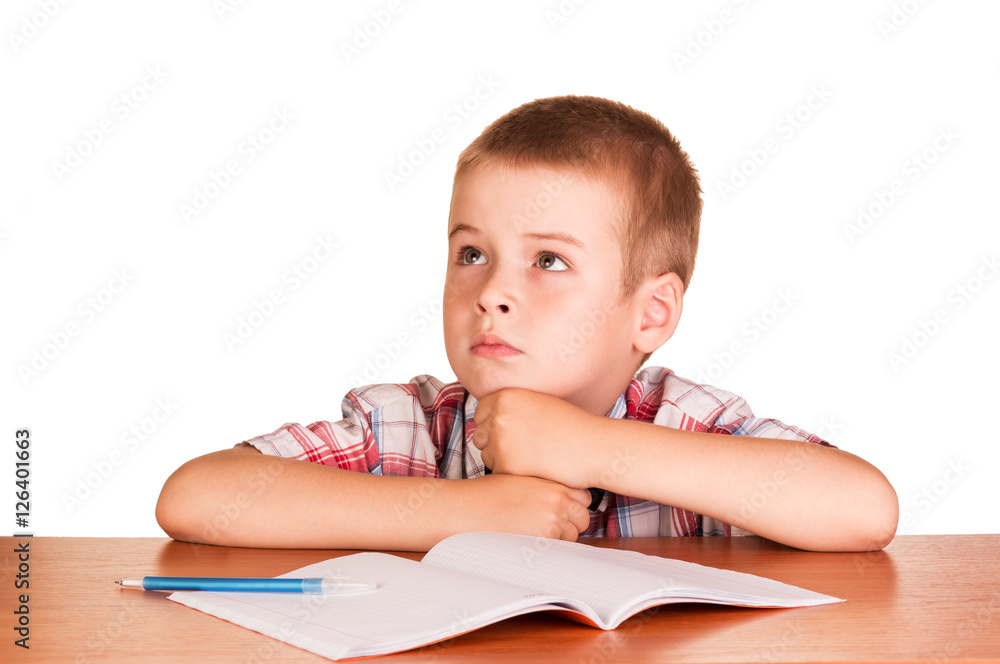 Dreamy boy sitting at table on notebook isolated white. Dreamy boy sitting at table on notebook isolated white.