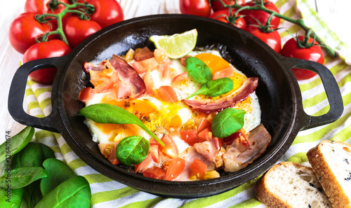 Pan of fried eggs with tomatoes, bacon, spinach, lime