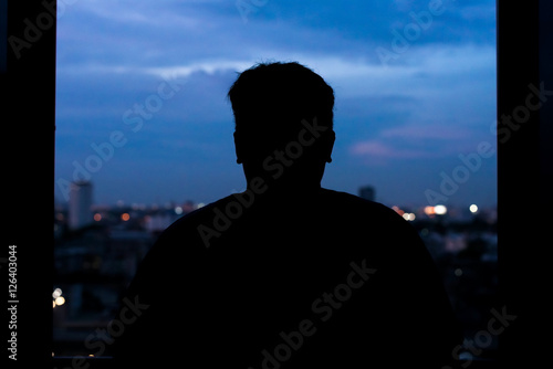 Man watching the view from skyscraper. Contours of the man to background night city. Black man silhouette in the window of a skyscraper. Dark outline man watching night city.