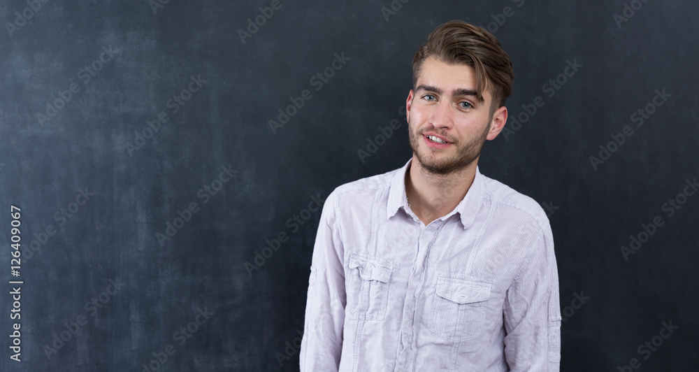 Handsome young student in shirt standing against blackboard