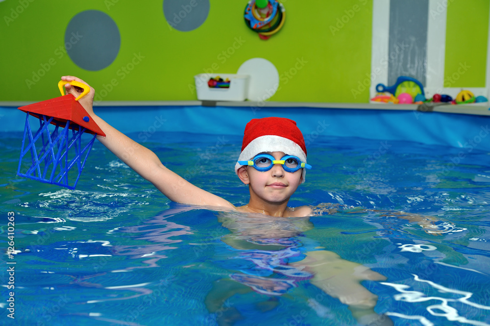 Child in hat Santa Claus swims in the pool on a blue background and looks at me. Portrait. The view from the top. Horizontal orientation
