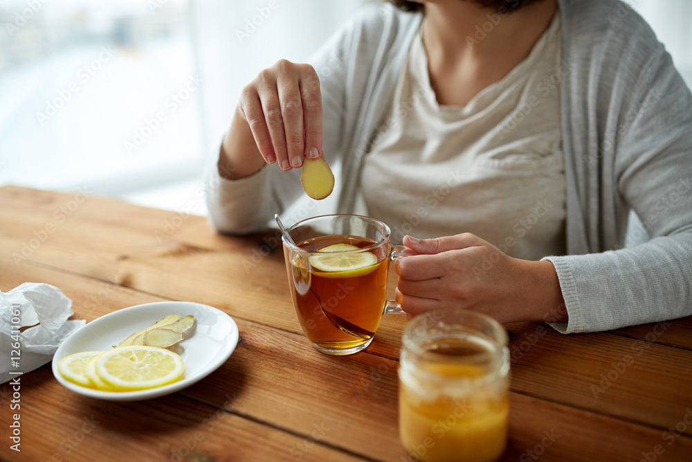 close up of woman adding ginger to tea with lemon close up of woman adding ginger to tea with lemon