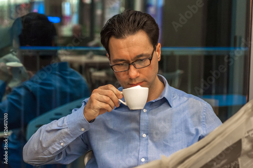 Young businessman sipping coffee and reading newspaper at cafe.