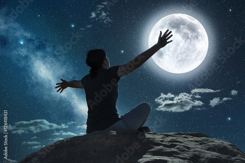 Fotografiet woman sitting and raising arms in the moonlight