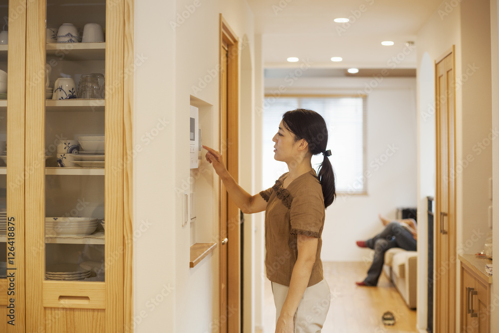 Family home. A woman adjusting the thermostat on a wall in the house. Family home. A woman adjusting the thermostat on a wall in the house.