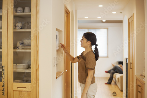 Family home. A woman adjusting the thermostat on a wall in the house. 