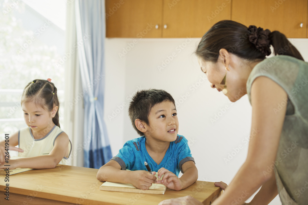 Teacher talking to two children sitting at desk Teacher talking to two children sitting at desk