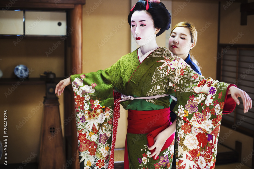 A woman being dressed in the traditional geisha style, wearing a kimono and  obi, with an