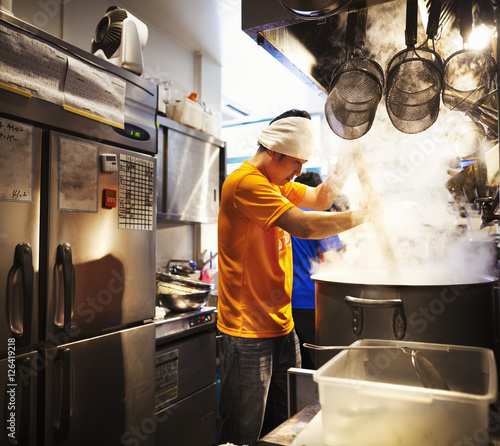 The ramen noodle shop, staff preparing food. Two men stirring a vat of noodles.  photo