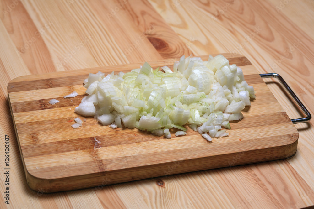Small cut onions lie on a board on a wooden table. Small cut onions lie on a board on a wooden table.