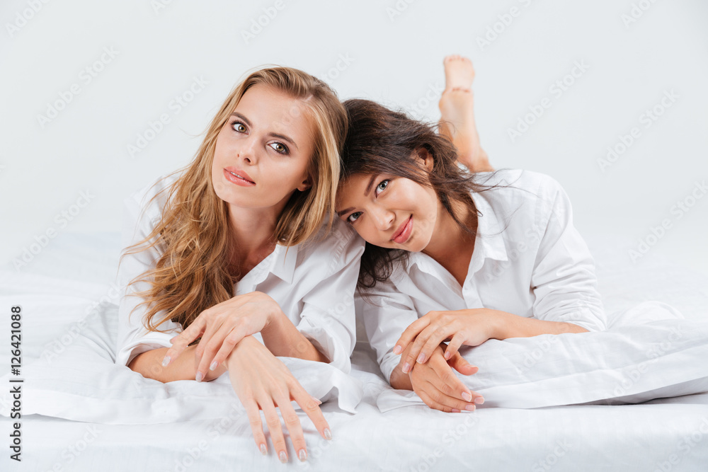 Two lovely girlfriends lying together on the bed with pillows Two lovely girlfriends lying together on the bed with pillows