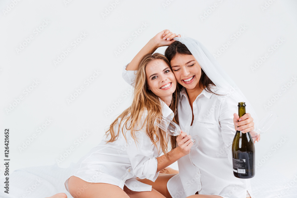 Fototapeta premium Two smiling women wearing bridal veil and holding champagne bottle