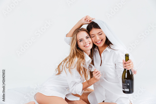 Tableau sur toile Two smiling women wearing bridal veil and holding champagne bottle