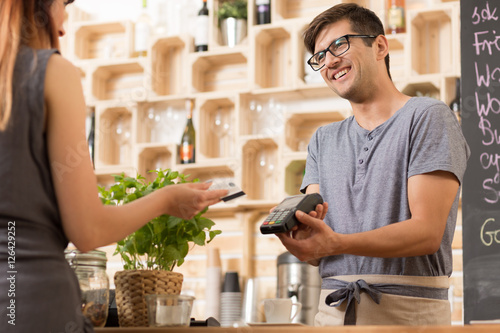 Foto Smiling barista with costumer paying by card