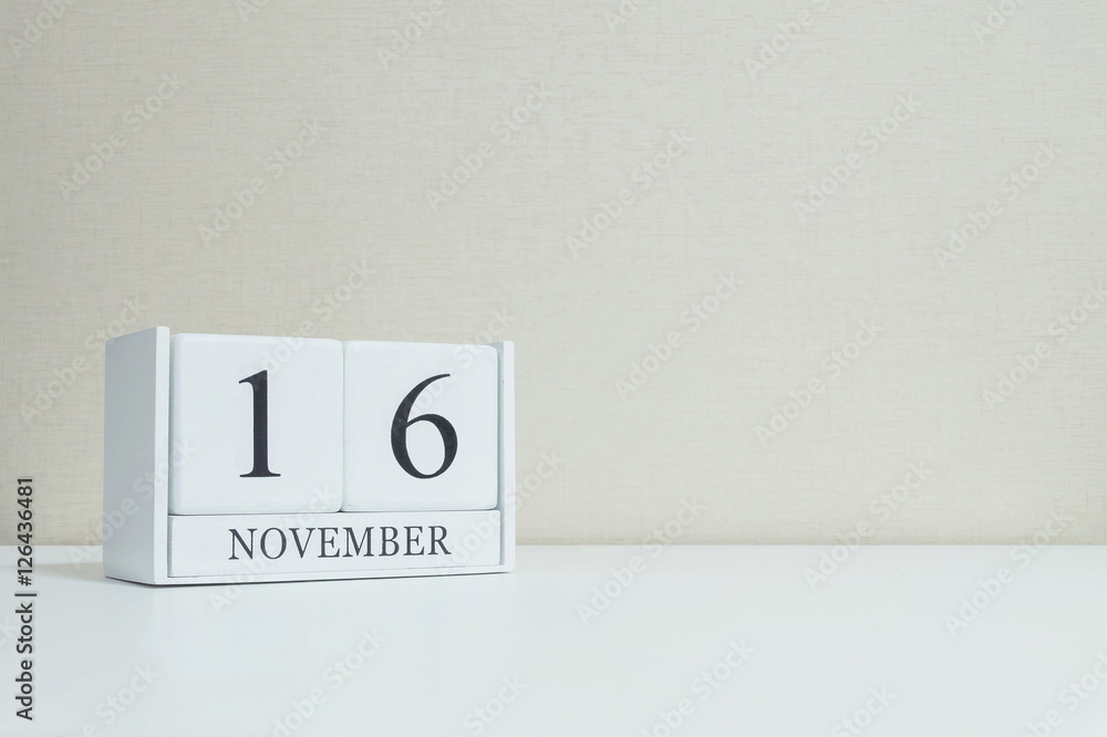 Closeup white wooden calendar with black 16 november word on blurred white wood desk and cream color wallpaper in room textured background with copy space , selective focus at the calendar Closeup white wooden calendar with black 16 november word on blurred white wood desk and cream color wallpaper in room textured background with copy space , selective focus at the calendar