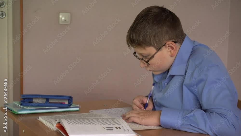 boy student writes in a notebook sitting at a desk