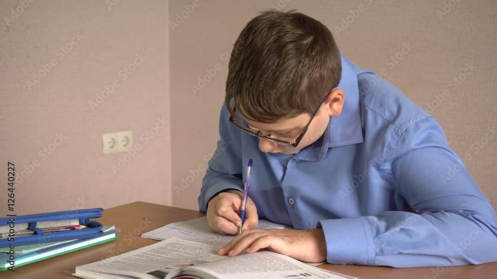 boy student writes in a notebook sitting at a desk boy student writes in a notebook sitting at a desk