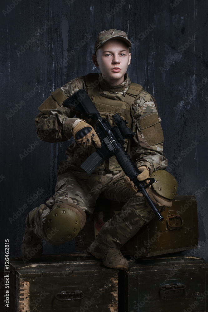 Fototapeta premium Portrait of a young soldier. The hands holding the rifle. Proud and confident quite complete.