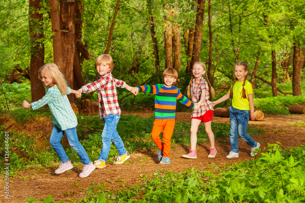 Five happy kids walking in forest holding hands