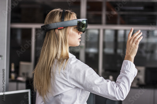 Virtual reality device. Woman playing game in virtual reality glasses. Headset  with virtual screen. Girl touch something using modern glasses with virtual screen.  photo