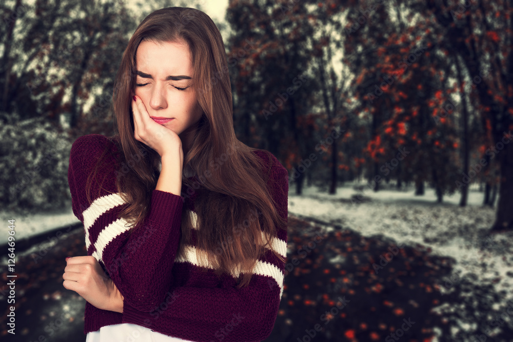 Portrait of a pretty woman having toothache standing over background of just came winter Portrait of a pretty woman having toothache standing over background of just came winter