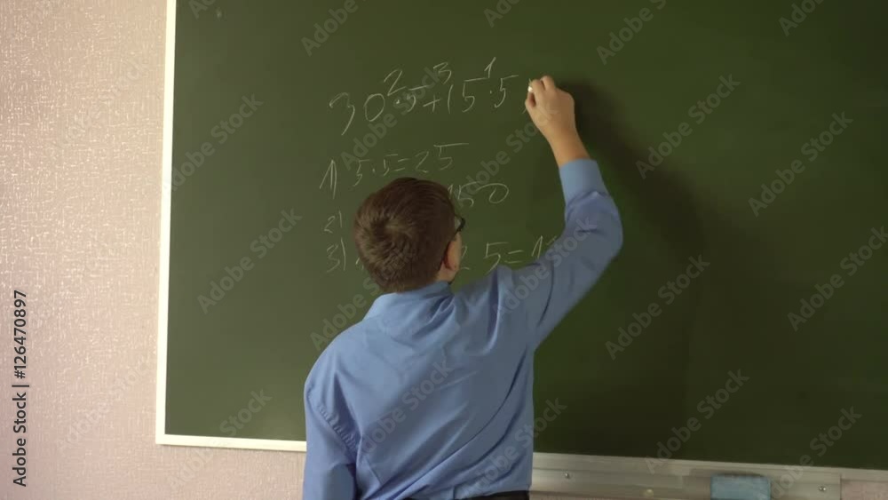 Teen student solves examples at the blackboard in the classroom Teen student solves examples at the blackboard in the classroom