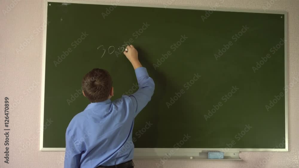 Teen student solves examples at the blackboard in the classroom Teen student solves examples at the blackboard in the classroom