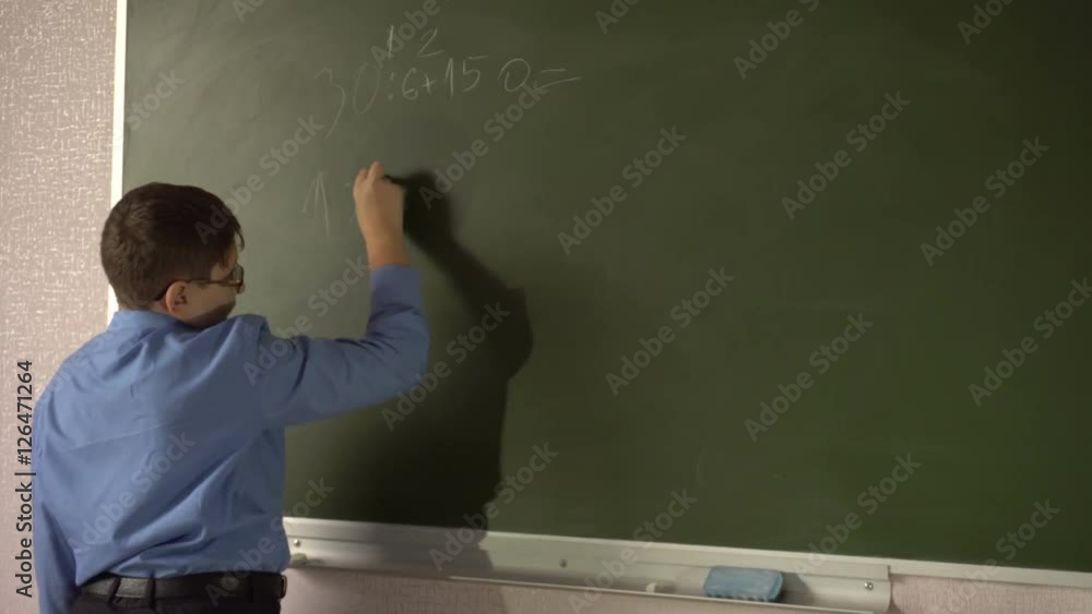 Teen student solves examples at the blackboard in the classroom Teen student solves examples at the blackboard in the classroom