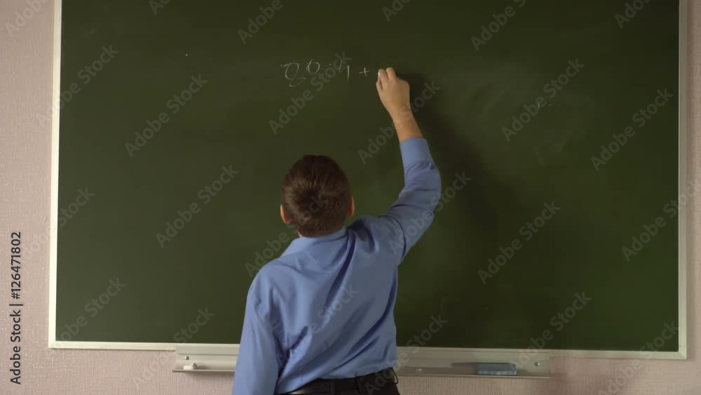 Teen student solves examples at the blackboard in the classroom Teen student solves examples at the blackboard in the classroom