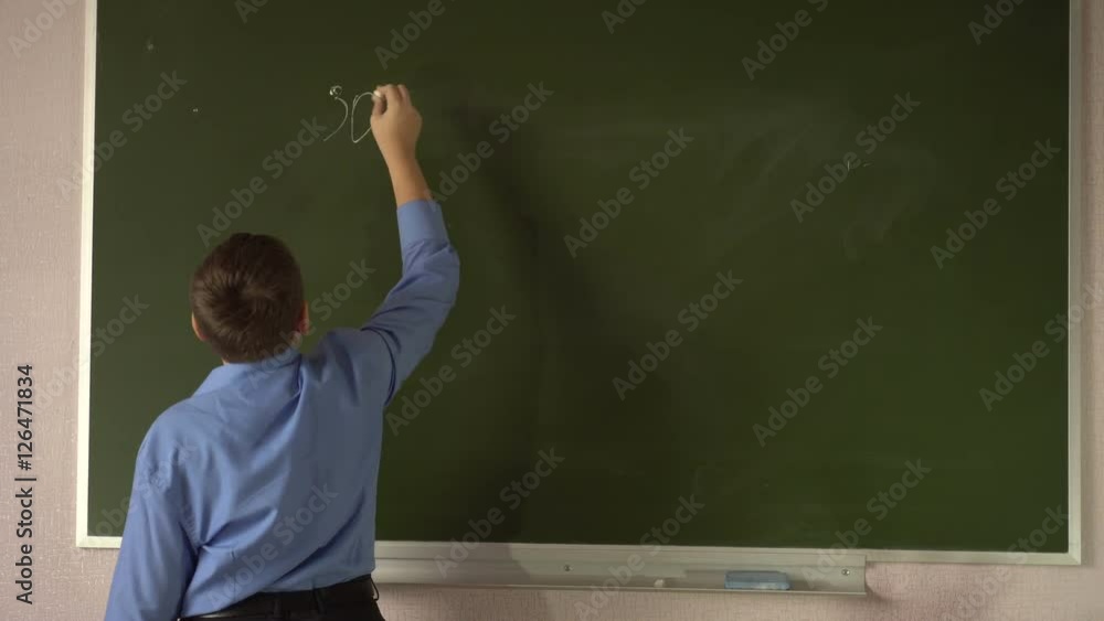 Teen student solves examples at the blackboard in the classroom Teen student solves examples at the blackboard in the classroom