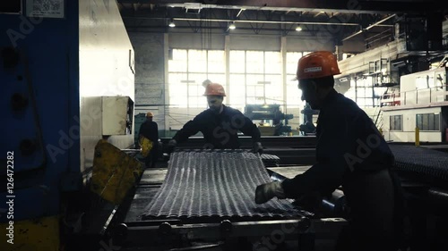two workers of the plant or factory lift sheet metal. Cling and crane hooks are on the machine for cutting metal blade photo