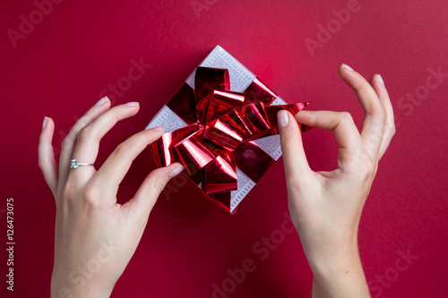 young woman girl hands holding wrapping white Christmas gift with shiny red ribbon on plain red background space for text
