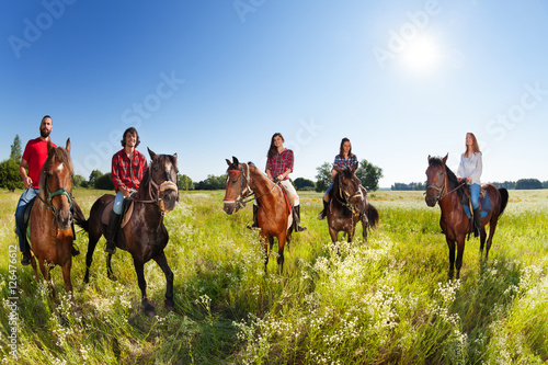 Group of five young people enjoy riding horses