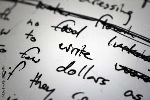 Lyrics written on paper in black ink close up. Focus on the word 