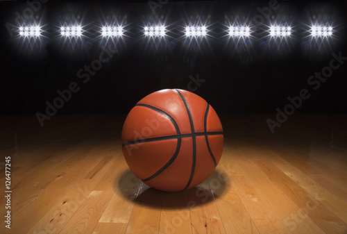Basketball on wood floor beneath bright lights