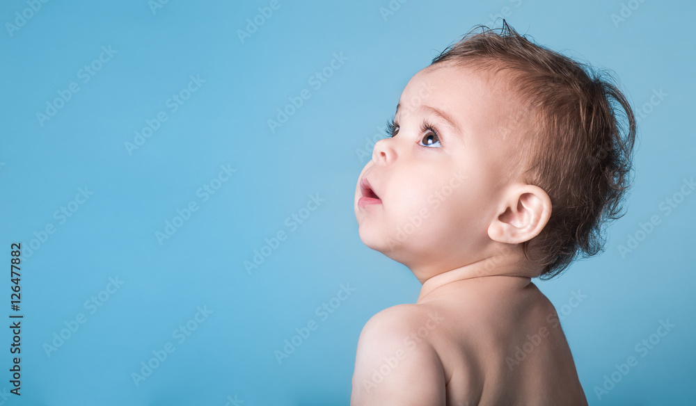 Cute Baby Girl Looking Up Against Vivid Blue Background - obrazy, fototapety, plakaty 