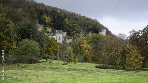 Gwrych Castle nestled in the trees on a hill side behind trees in Wales - European castle in the UK during Autumn - stormy weather and clouds