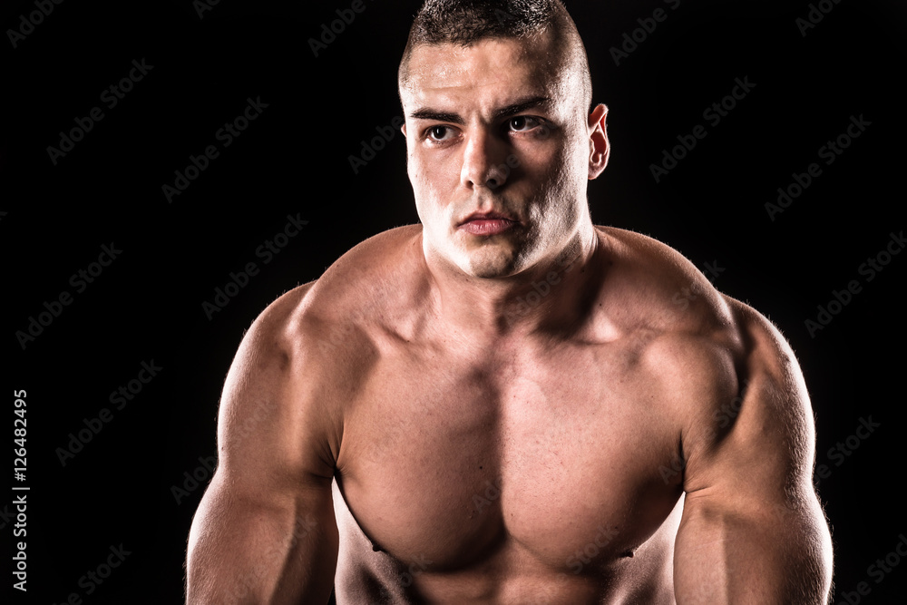Fototapeta premium Young bodybuilder man stretching muscles on a black background