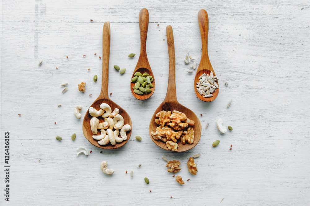 Four wooden spoons with seeds and nuts on thw white table