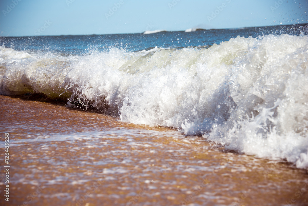 Fototapeta premium Sea wave breaking on the beach in a sunny day