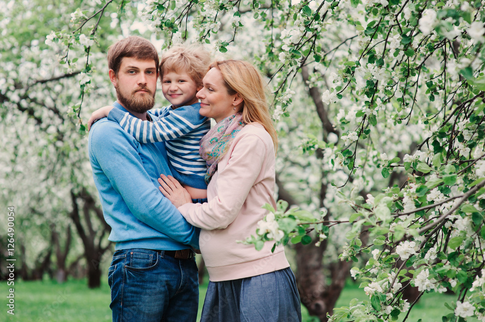 spring portrait of happy family enjoying holidays in blooming garden. Pregnant mother, father and son walking together outdoor spring portrait of happy family enjoying holidays in blooming garden. Pregnant mother, father and son walking together outdoor