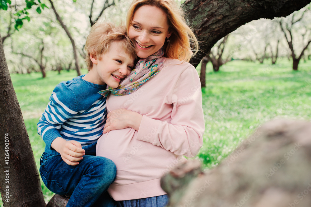 spring portrait of happy pregnant mother enjoying warm day with child son in blooming apple garden spring portrait of happy pregnant mother enjoying warm day with child son in blooming apple garden